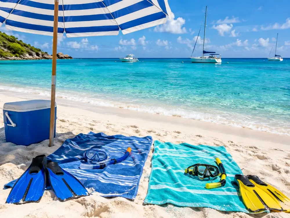 A beach umbrella, towels, snorkel masks and a cooler on white sand